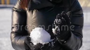 一个戴手套的女孩拿着雪球。 手拿雪。 在晴朗的冬天玩雪球。 冬季概念。
